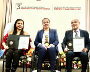 En la imagen al centro la Ing. Miriam García Zamora, a su derecha Mineva Ramos García sosteniendo en la mano derecha la medalla conmemorativa y en la mano izquierda un reconocimiento del Premio Retos y Razones 2021, y al lado izquierdo de la Ing. Garcíz Zamora, el Maestro Martín Dones, representando a la Organización Civil "CECADEE la Luz", recibiendo de igual forma, la medalla y el reconocimiento del premio.